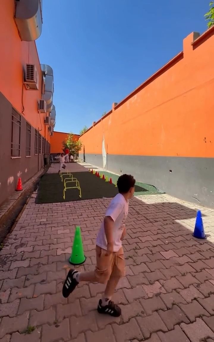 Turuncu duvarlı bahçedeki koni parkurunda koşan öğrenci